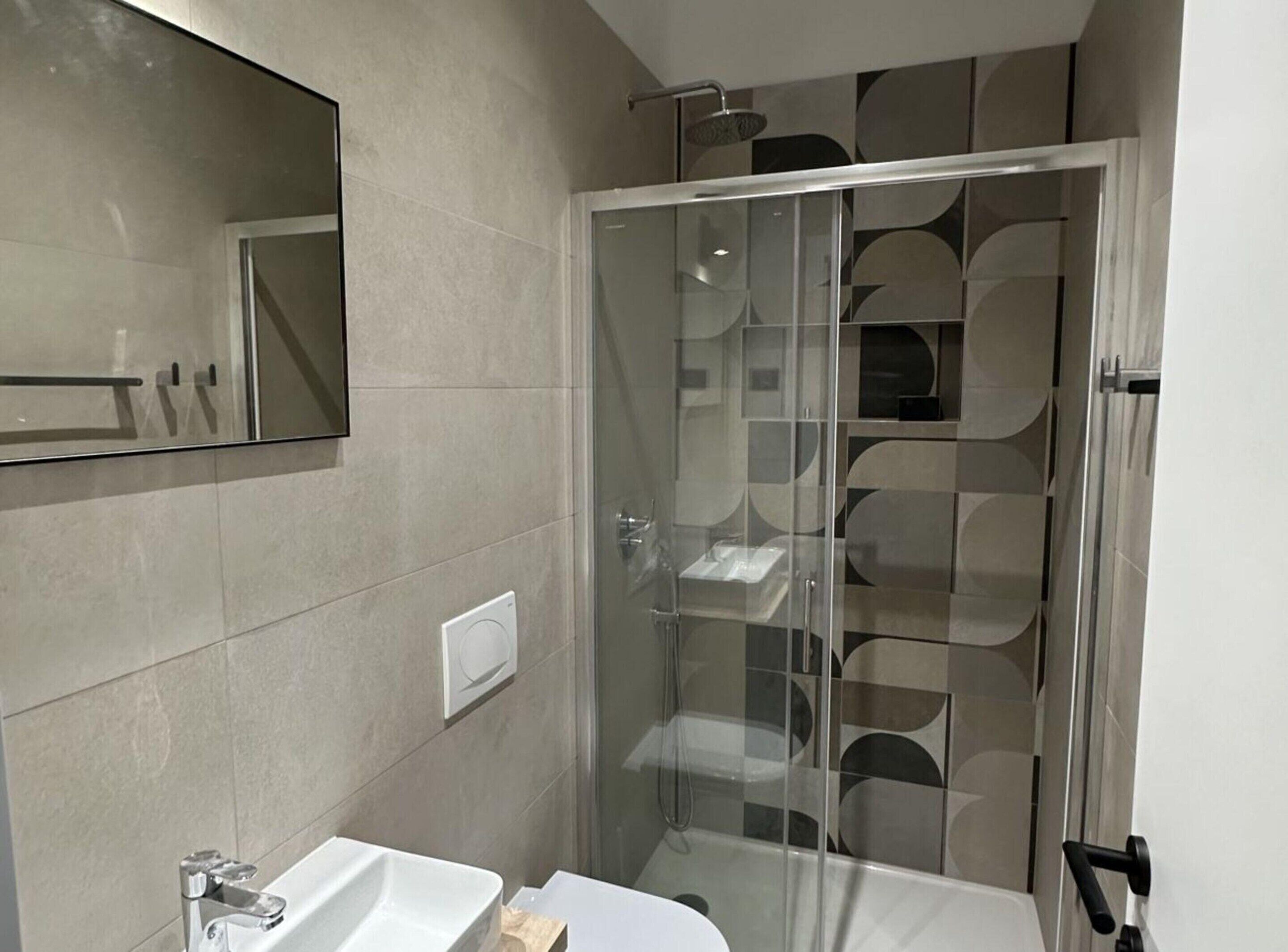 A modern bathroom with a glass-enclosed shower, a white sink, and a large mirror.