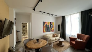 A modern living room with a sofa, armchair, coffee table, and a TV mounted on the wall. - Apartment Urban Living (Porec)