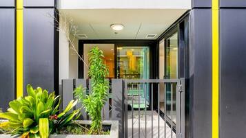 A modern building entrance with a gated driveway, a potted plant, and a visible interior space with a dining area.