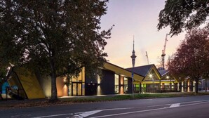 A modern building with a glass facade, a prominent tower in the background, and a well-lit entrance area. - Stunning and Serene Two-bedroom Apartment (Auckland)