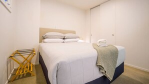 A hotel room with a bed, a bedside table, a wall-mounted drying rack, and a wardrobe. - Stunning and Serene Two-bedroom Apartment (Auckland)