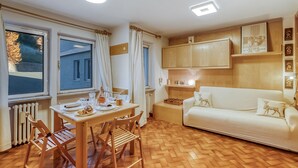 Een knus vertrek met een houten vloer, een eettafel met stoelen, een witte bank en een radiator.