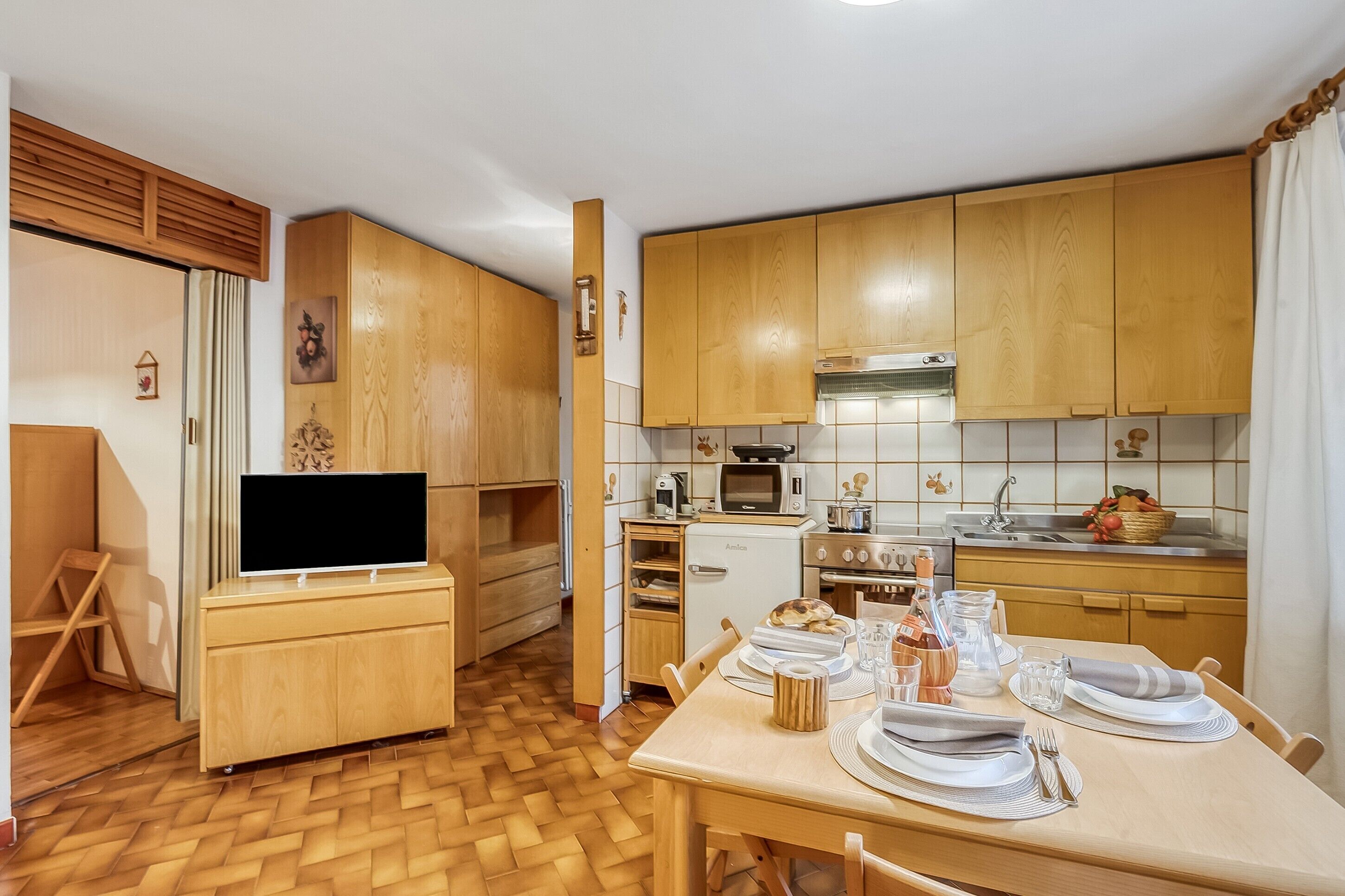 Eine kleine Küche mit Holzausstattung, einem Esstisch für zwei Personen und einem Fernseher auf einem Schrank.