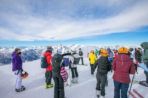 Un grupo de personas en la cima nevada de una montaña, probablemente preparándose para esquiar o hacer snowboard.