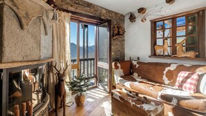 A rustic interior with a stone wall, a wooden sofa, a fireplace, and a view of mountains through a large window. - Grange Romantic Retreat Mountain View (Sauze di Cesana)