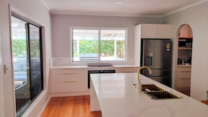 A modern kitchen with a large island, white cabinetry, a stainless steel refrigerator, and a window with a view of greenery.