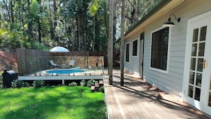A backyard with a wooden deck, a swimming pool, and a fenced area with chairs and umbrellas.