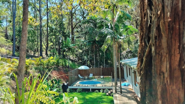 A backyard with a wooden deck, a swimming pool, and a fenced area with chairs and a table.