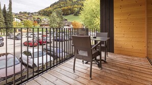 A balcony with wicker chairs and a table, overlooking a parking lot and a mountainous landscape.