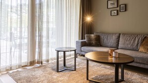 A living room with a sofa, two tables, a rug, and a large window with sheer curtains.