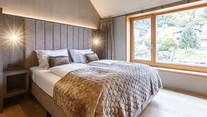A modern bedroom with a large bed, a wooden headboard, and a view of a residential area through a large window.