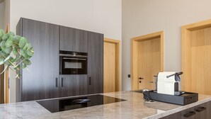 A modern kitchen with dark wood cabinets, a built-in oven, a coffee machine, and a marble countertop.