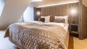 A modern bedroom with a hexagonal patterned bedspread, a wooden headboard, and a sloped ceiling.