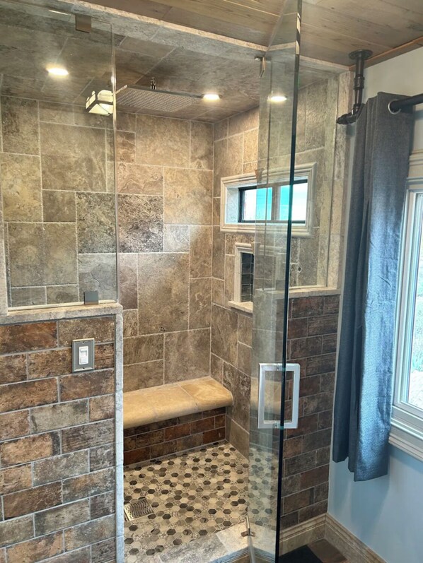 A shower area with a glass partition, stone tiles, and a bench.