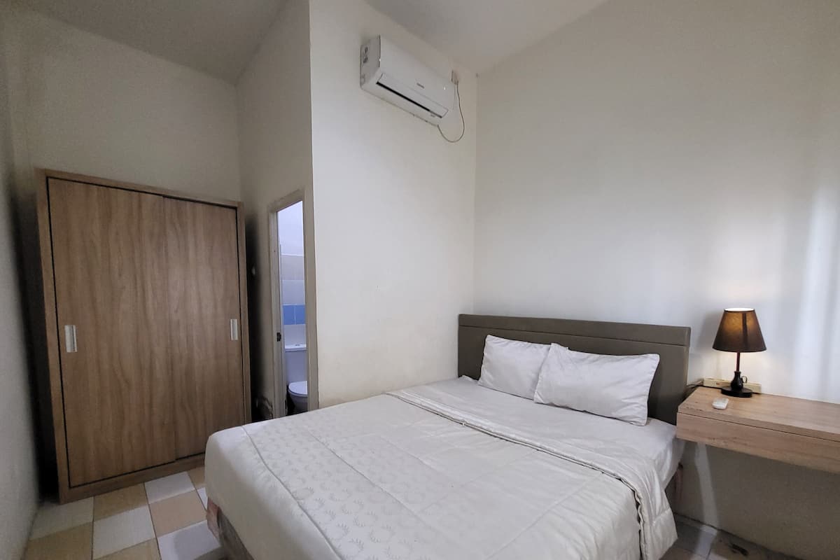 Un dormitorio con cama, armario de madera, mesita de noche con lámpara y equipo de aire acondicionado en la pared.
