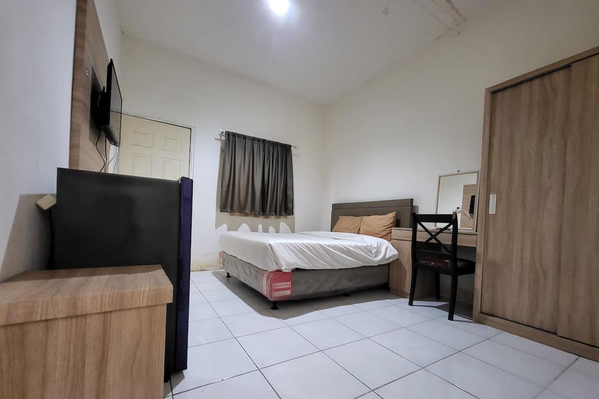 Un dormitorio con cama, armario de madera, escritorio, silla, televisor y ventana con cortinas.