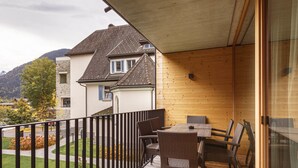 Eine Holzdar Terrasse mit Tisch und Stühlen, mit Blick auf einen Garten und ein Gebäude mit Schrägdach.