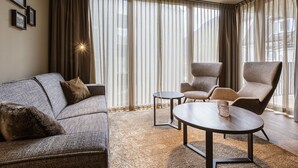 Ein modernes Wohnzimmer mit einem grauen Sofa, zwei Sesseln, einem kleinen runden Tisch und transparenten Vorhängen.