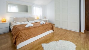 A bedroom with a large bed, a wardrobe, a nightstand with a lamp, and a white rug.
