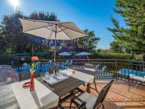 An outdoor patio with a table set for dining, surrounded by chairs and a large umbrella. - Scenic Villa With Private Garden (Porec)