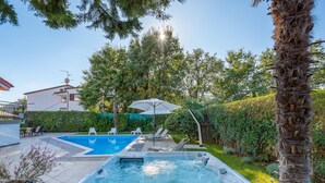 A backyard with a hot tub, a swimming pool, and lounge chairs.