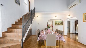 A dining area with a table set for four, a staircase, and an air conditioning unit on the wall.