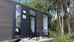 A modern, compact cabin with a wooden deck and two chairs. - The Dacious by Tiny Away (East Feluga)