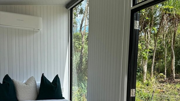 A bedroom with a bed, pillows, a blanket, and a view of the outdoors through large windows. - The Dacious by Tiny Away (East Feluga)