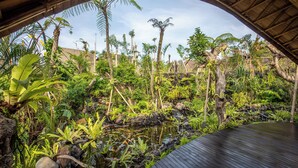 A tropical garden with a pond, lush greenery, and a wooden deck. - E Sanctuary Resort Ubud (Ubud)