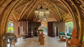 A room with a high, arched bamboo ceiling, a central chandelier, a wooden bench, a sofa, and a decorative sculpture. - E Sanctuary Resort Ubud (Ubud)