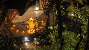 An outdoor dining area with a table and chairs, surrounded by candles and tropical plants. - E Sanctuary Resort Ubud (Ubud)