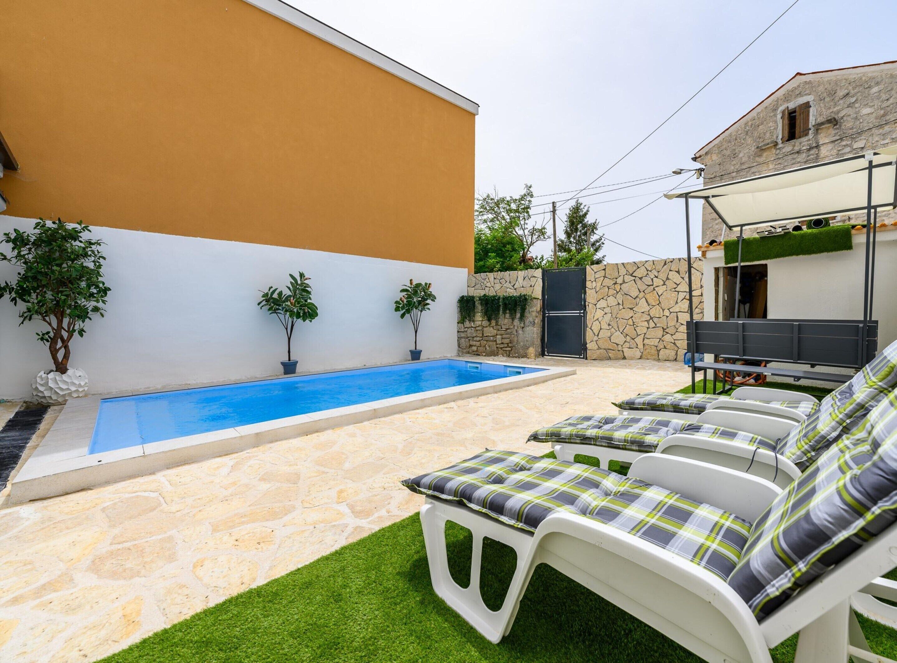 Zona de piscina amb paviment de pedra, paret blanca i un petit jardí amb plantes en testos.