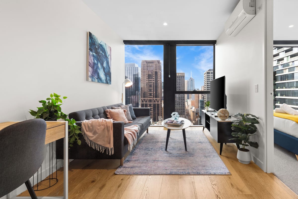 Ein modernes Wohnzimmer mit einer Couch, einem Couchtisch und Pflanzen. Ein großes Fenster bietet Blick auf die Stadt.