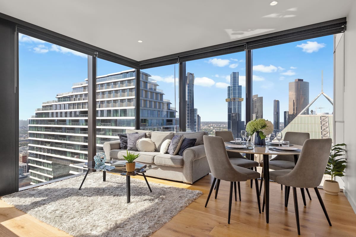 Ein modernes Wohnzimmer mit großem Fenster, einer Couch, einem Esstisch mit Stühlen und Blick auf die Stadt.