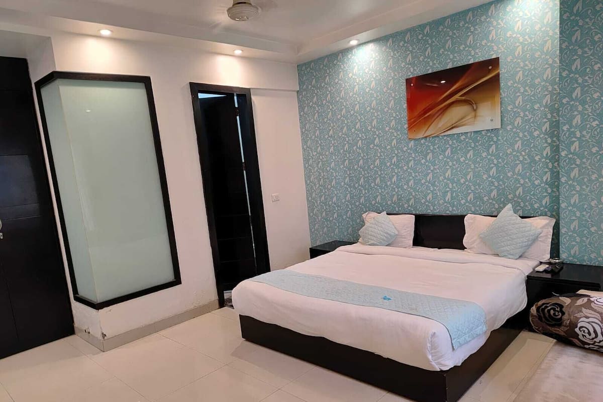 Ein Schlafzimmer mit einem Bett, einem Nachttisch, einem Wandbild und einer gemusterten Wand.