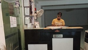 A reception desk with a sign labeled "RECEPTION" and a person seated behind it. - Hotel Swathi  (New Delhi)