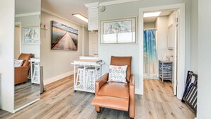 A spacious room with a brown leather chair, a white desk, and a large mirror. There are framed pictures on the walls and a view of the outside. - 114 Beachfront Heated Pool Studio Harborside View (Galveston)
