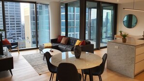 A modern living room with a sofa, a round table, and a kitchen area. - Melbourne Corporate Apartments – Collins Street (Melbourne)