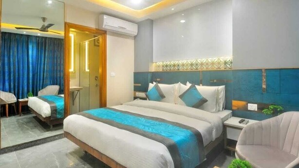 A modern hotel room with a large bed, bedside tables, a chair, and a mirror. - HOTEL IMPERIAL VIEW (New Delhi)