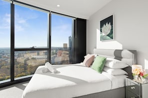 A modern bedroom with a large window, a bed with white linens, and a city view. - Melbourne Corporate Apartments - King Street (Melbourne)