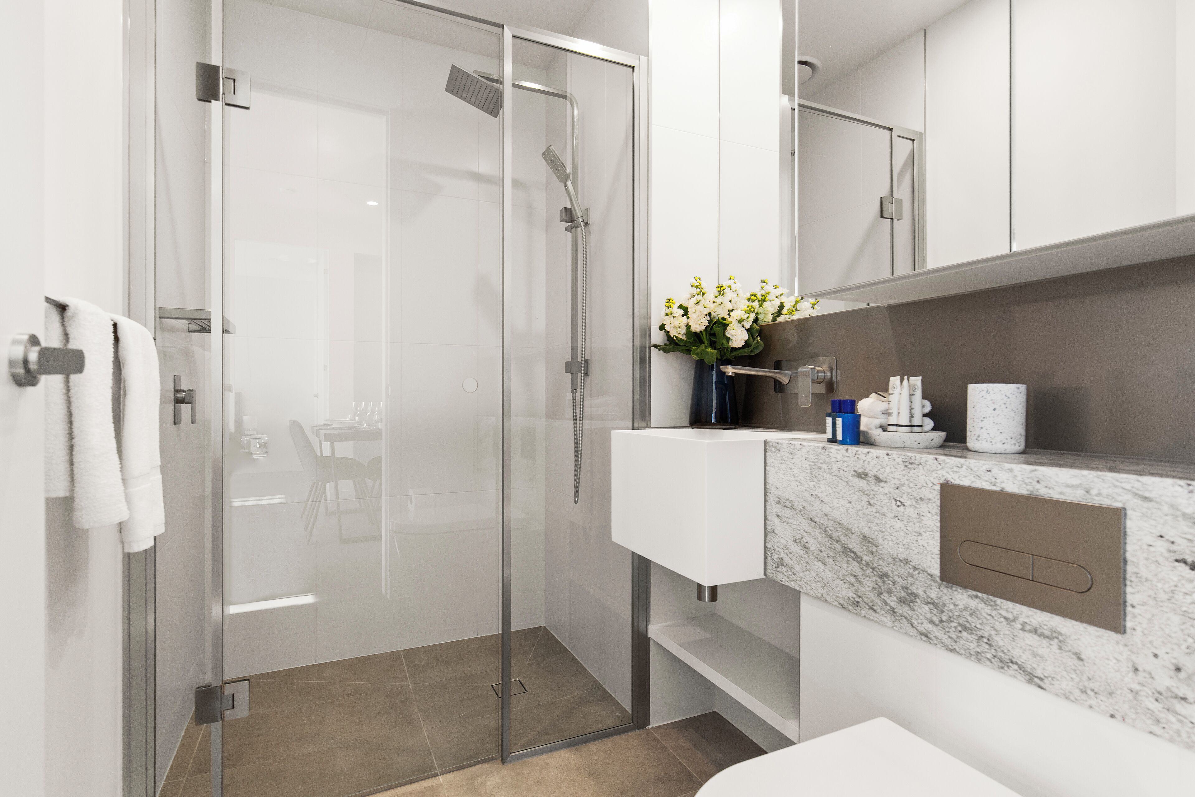 A modern bathroom with a glass-enclosed shower, a white sink, and a marble countertop.