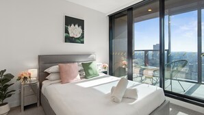Een moderne hotelkamer met een groot bed, een nachtkastje met een lamp en een balkon met uitzicht op de stad.