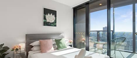 A modern hotel room with a large bed, a nightstand with a lamp, and a balcony with a city view.