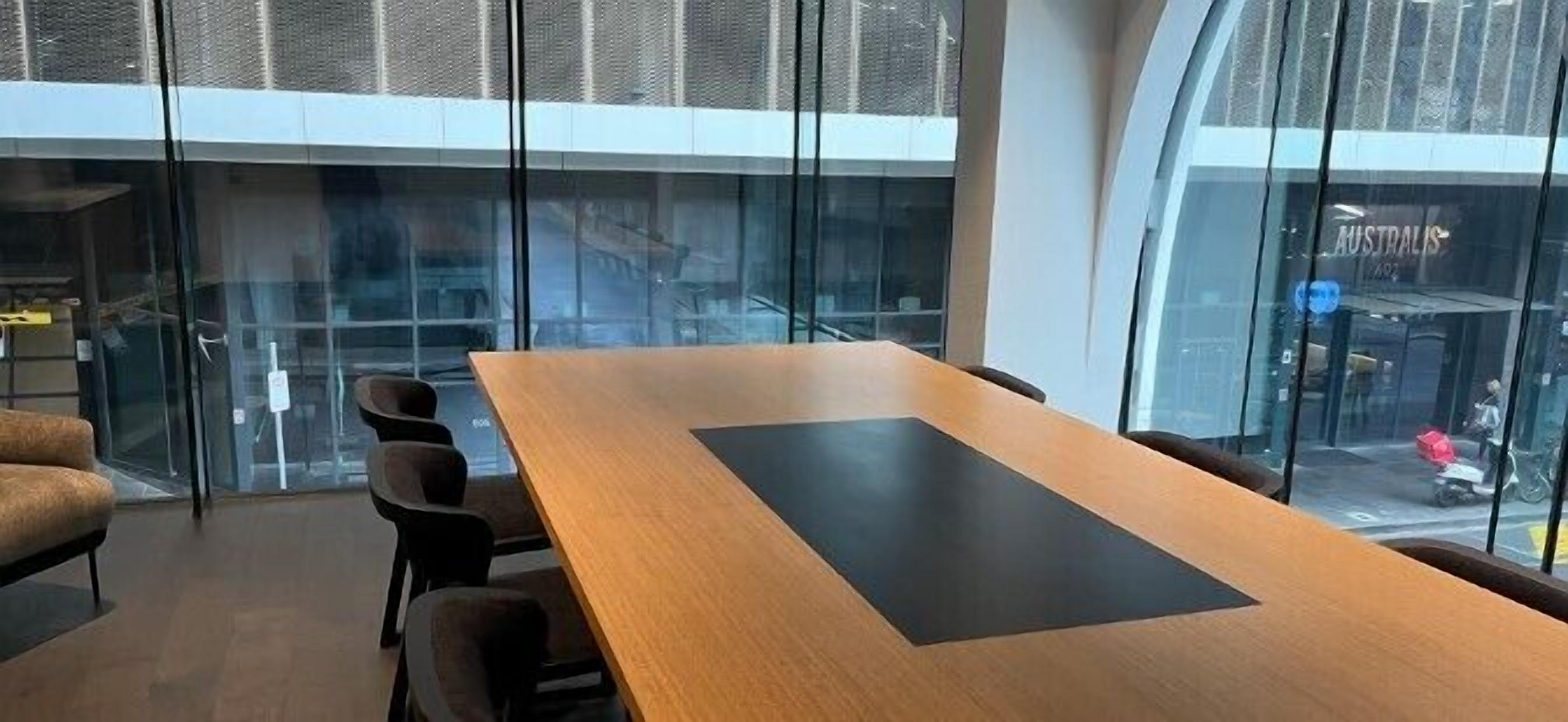 A conference room with a long table and chairs, large windows, and a view of the street outside.
