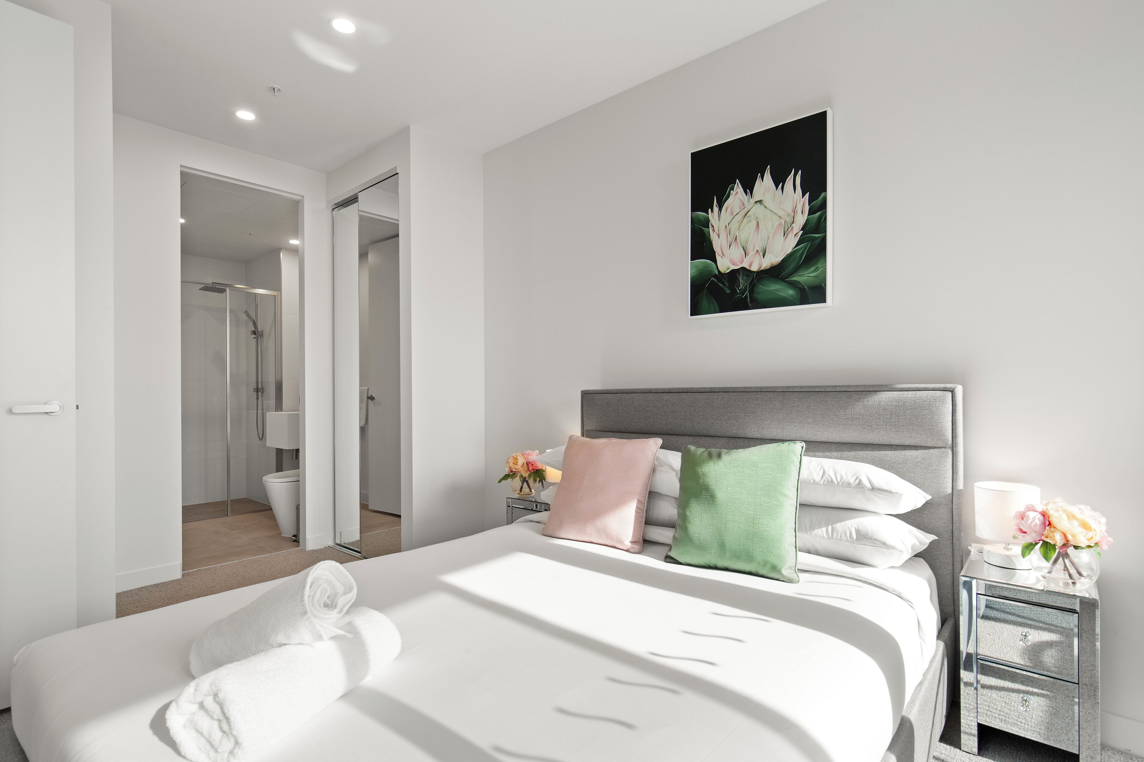 Een moderne hotelkamer met een groot bed, een nachtkastje met een lamp en een kunstwerk in een lijst aan de muur.