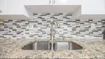 A kitchen with a double sink, granite countertop, white cabinets, and a mosaic backsplash.