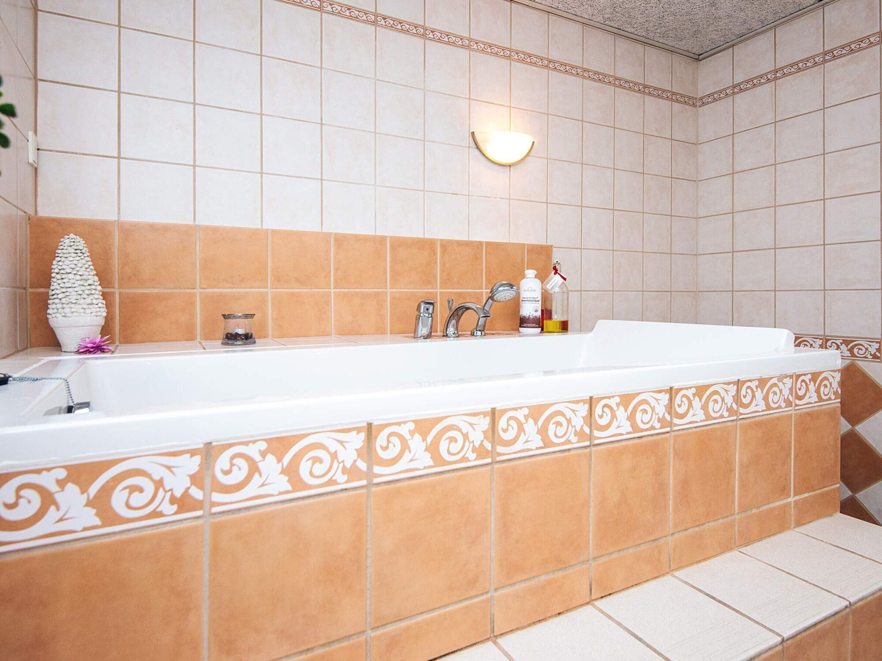 A bathroom with a white bathtub, a wall-mounted light, and a decorative plant.