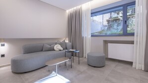 Un salon moderne avec un canapé gris, un petit pouf rond, une table basse et une fenêtre avec des rideaux.