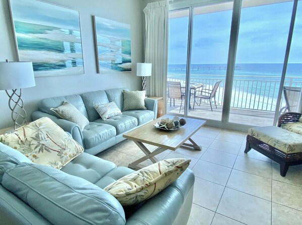 A spacious living room with a large sofa, a coffee table, and a balcony with a view of the ocean.