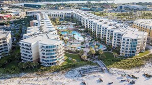 A beachfront hotel with multiple buildings, a central pool area, and a beach with sun loungers.